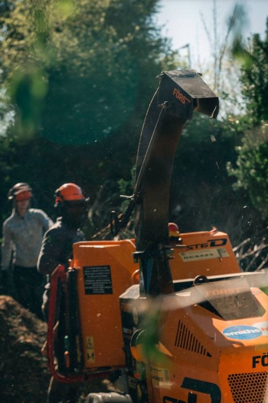 Two of the team in helmets beside a woodchipper during the Unsworth clearance